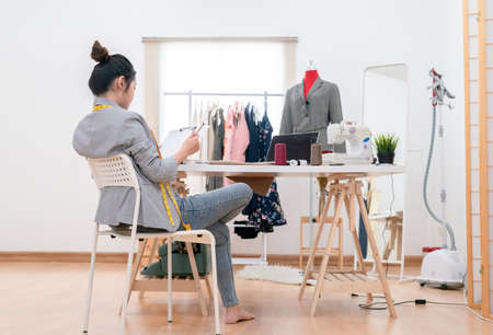 Beautiful asian woman fashion designer tailor fabric working and sewing her sketch clothes design to customer, creative in studio tailor shop, occupation owner small business conceptの写真素材