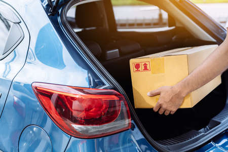 Delivery man carrying cardboard box for sending deliver to customer by transportation system hatchback car, Business of male transport sell part or product service parcel for convenience of customerの写真素材