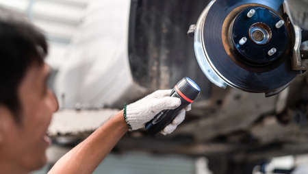 Mechanic man examining and service maintenance the disk brake of a vehicle with flashlight, Safety inspection test engine before customer drive a car on a long journey, transportation serviceの写真素材