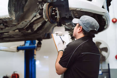 Mechanic asian man examining and service maintenance the suspension of a vehicle, Safety inspection test engine before customer drive a car on a long journey, transportation serviceの写真素材