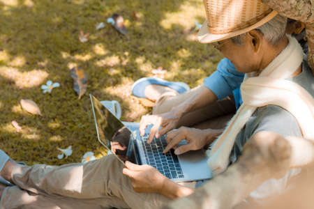 Happy family asian senior couple using laptop computer technology retirement smile in nature park relax vacation time, Elderly romantic valentine lover leisure activity healthy people lifestyleの写真素材