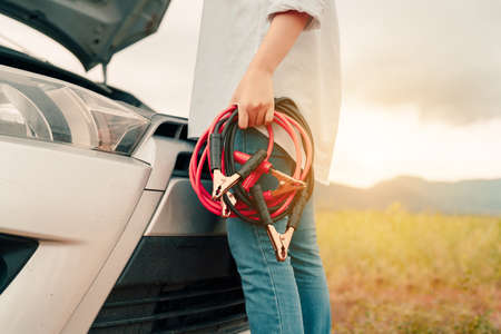 Close up Woman connecting battery cable copper wire for jumper repair and maintenance electric of engine car problem, broken her self service transportation, Vehicle stop engine between travelの写真素材