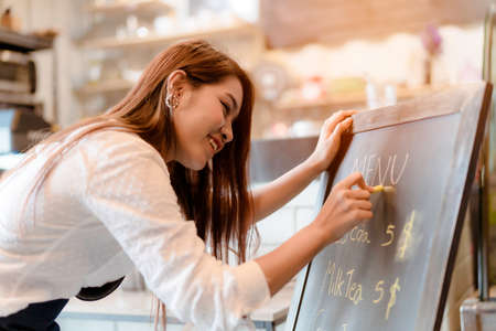 Asian woman Barista writing menu front counter coffee shop occupation, part-time,job or owner business working woman happy selling and making drink beverageの写真素材