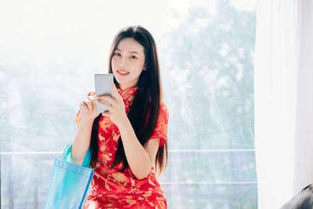 Beauty Asian Woman with Chinese dress,Qipao,Cheongsam Chinese New Year Using Smartphone Technology Shopping Online Standing near Window in Clean White Room,Copy Space.の写真素材