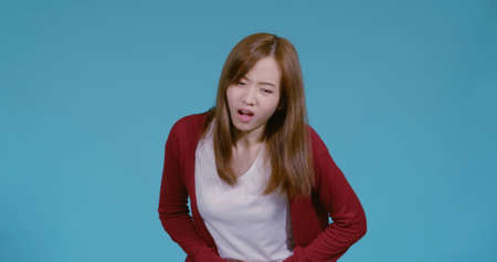 Young asian woman stomach ache or abdominal pain reaction in t-shirt and wrapper healthy sick concept on blue background isolated studio shot.の写真素材