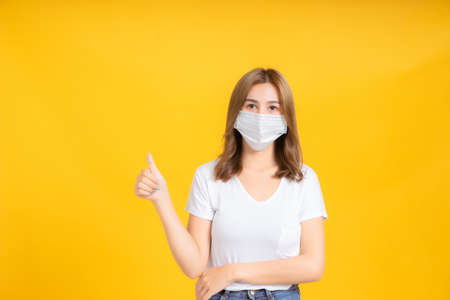 Asian women thumbs up wear correct masks to protect against germs from coronavirus, covid-19, pm2.5 dust and prevent infections on a yellow background, healthy concept.の写真素材