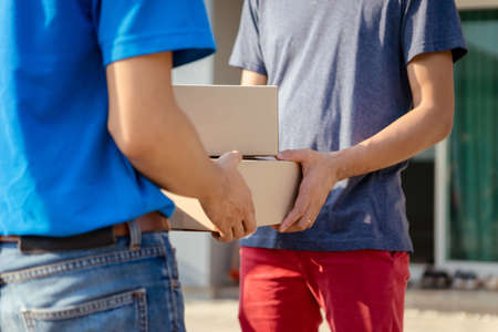 Close up Delivery man wearing mask send a package holding parcel cardboard on front receiver...