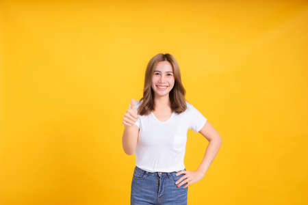 Portrait happy young asian woman smiling thumbs up good hand gesture positive emotion in white t-shirt, Yellow background isolated studio shot and copy space.の写真素材
