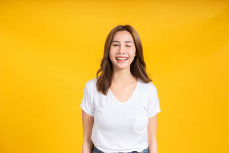 Portrait happy young asian woman laughing blink, wink eye joyful funny positive emotion in white t-shirt, Yellow background isolated studio shot and copy space.の写真素材