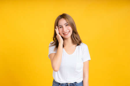 Portrait happy young asian woman smiling hand holding ear listening something positive emotion in white t-shirt, Yellow background isolated studio shot and copy space, gossip secret concept.の写真素材