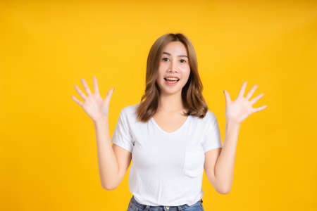 Portrait happy young asian woman glad open hands smiling positive emotion in white t-shirt, Yellow background isolated studio shot and copy space.の写真素材
