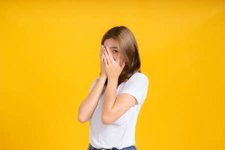 Portrait young asian woman covered your hide eye peek looking, scary watching horror movie in white t-shirt, Yellow background isolated studio shot and copy space.の写真素材