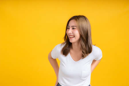 Portrait young happy asian woman smile laughing standing enjoy fun relaxing carefree positive emotion in white t-shirt, Yellow background isolated studio shot and copy space.の写真素材
