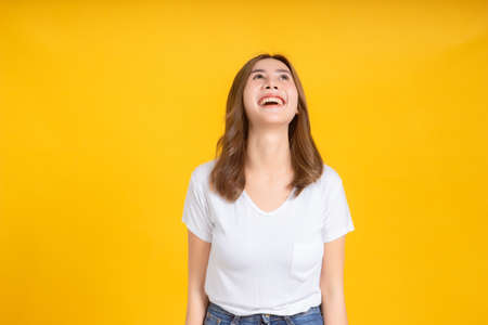 Portrait young happy asian woman smile laughing standing enjoy fun relaxing carefree positive emotion in white t-shirt, Yellow background isolated studio shot and copy space.の写真素材