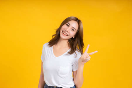 Portrait happy young asian woman laughing finger hands v-symbol gesture selfie joyful funny positive emotion in white t-shirt, Yellow background isolated studio shot and copy space.の写真素材