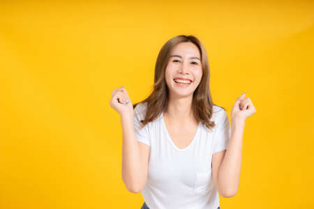 Portrait happy young asian woman dancing music celebrate fun enjoyment relaxation smiling positive emotion in white t-shirt, Yellow background isolated studio shot and copy space, party concept.の写真素材
