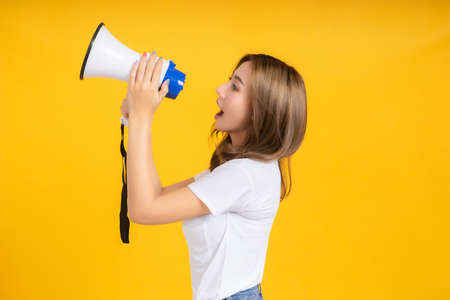 Speaking Loud noise announce of young asian woman with megaphone promotional advertising in white t-shirt smiling emotion on yellow background isolated studio shot with copy space.の写真素材