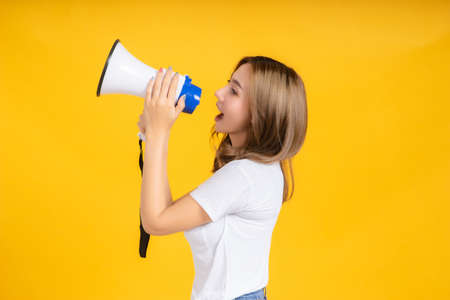 Speaking Loud noise announce of young asian woman with megaphone promotional advertising in white t-shirt smiling emotion on yellow background isolated studio shot with copy space.の写真素材
