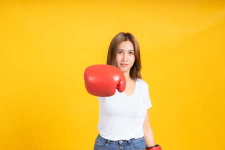 Portrait happy young asian woman with boxing glove punching hit or self defend in white t-shirt, Yellow background isolated studio shot and copy space.の写真素材