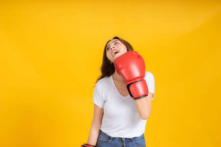 Portrait happy young asian woman with boxing glove  self business knock out, punching hit in white t-shirt, Yellow background isolated studio shot and copy space.の写真素材