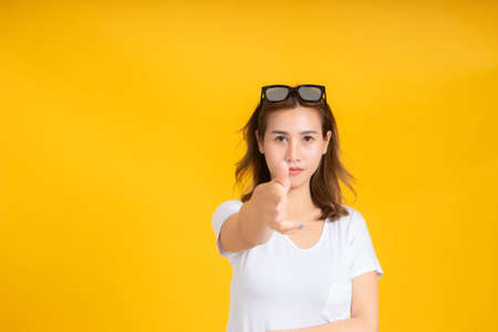 Portrait young asian woman gun shot hand gesture emotion killing business in white t-shirt, Yellow background isolated studio shot and copy space.の写真素材