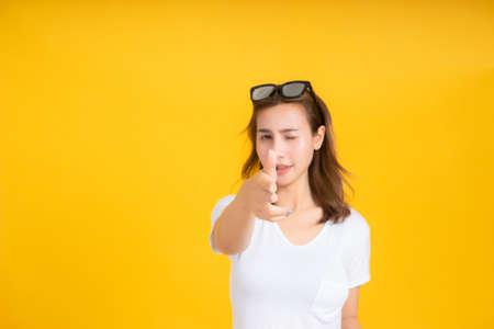 Portrait young asian woman gun shot hand gesture emotion killing business in white t-shirt, Yellow background isolated studio shot and copy space.の写真素材