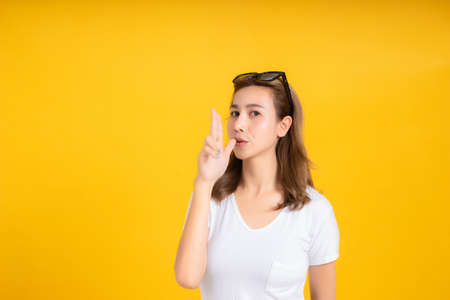 Portrait young asian woman gun shot hand gesture emotion killing business in white t-shirt, Yellow background isolated studio shot and copy space.の写真素材