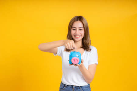 Portrait happy young asian woman holding piggybank saving money for future and business earning income positive emotion in white t-shirt, Yellow background isolated studio shot and copy space.の写真素材