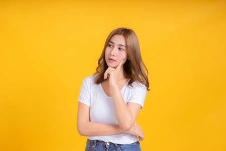 Portrait young asian woman thinking thought looking inspiration for idea working business in white t-shirt, Yellow background isolated studio shot and copy space.の写真素材