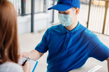 Door to door delivery express sending send a package wearing mask to customer receiver sign checking...