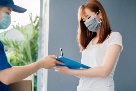 Door to door delivery express sending send a package wearing mask to customer receiver sign checking shipping deliver cargo prevention infection quarantine while the virus is spreading, Coronavirus.の写真素材