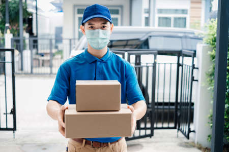 Asian Delivery man wearing mask send a package carton on front receiver shipping deliver social distancing while the virus is spreading and prevention crisis coronavirus covid-19 front home customer.の写真素材