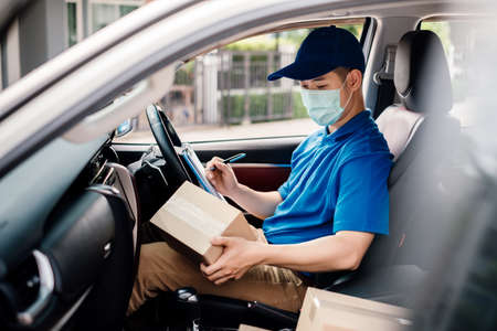 Asian Delivery man wearing mask picking up the package and checking to front home receiver shipping deliver cargo social distancing, Many parcel in car while the virus is spreading quarantine.の写真素材
