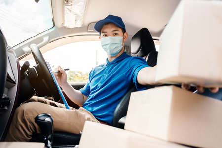 Asian Delivery man wearing mask picking up the package and checking to front home receiver shipping deliver cargo social distancing, Many parcel in car while the virus is spreading quarantine.の写真素材