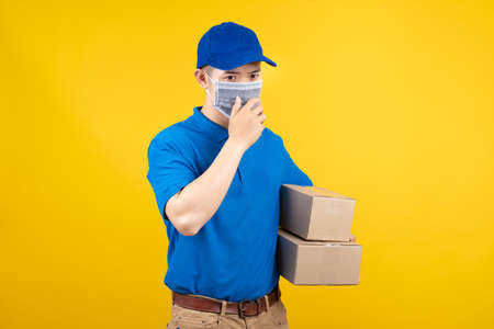 Delivery handsome asian man wearing mask patient wearing mask dry cough have fever quarantine infection courier package to customer risk get infected on yellow background studio shot with copy space.の写真素材