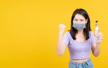 Portrait asian woman wearing mask with hand sanitizer alcohol gel for protection against germs from coronavirus, Glad excited covid-19 and prevent infections on yellow background isolated.の写真素材