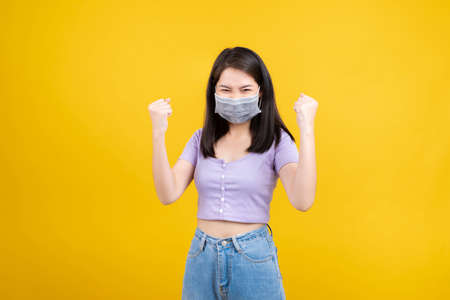 Studio shot Portrait asian woman wearing mask protection against germs from coronavirus and prevent infection, Glad excited emotion after recover from illness covid-19 on yellow background isolated.の写真素材
