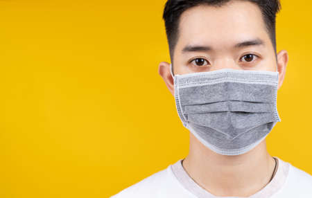 Close up Face of man wearing medical mask protection against germs from crisis coronavirus, covid-19 and prevent infection on yellow background isolated studio shot with copy space the left.の写真素材