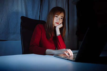 Asian woman working late at night with laptop computer home office looking screen monitor unhappy work hard, Freelancer stay home business quarantine sleepless crisis coronavirus in dark room.の写真素材