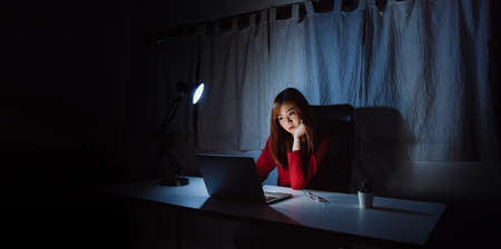 Asian woman working late at night with laptop computer home office looking screen monitor unhappy work hard sleepless, Freelancer stay home business quarantine crisis coronavirus in dark room.の写真素材