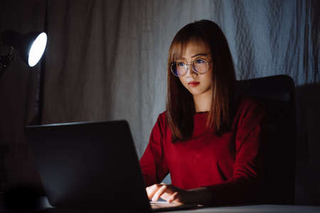 Asian woman working late at night with laptop computer home office looking screen monitor unhappy work hard sleepless, Freelancer stay home business quarantine crisis coronavirus in dark room.の写真素材