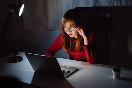 Asian woman working late at night with laptop computer home office looking screen monitor unhappy work hard sleepless, Freelancer stay home business quarantine crisis coronavirus in dark room.の写真素材