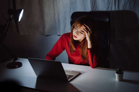 Asian woman working late at night with laptop computer home office looking screen monitor unhappy work hard sleepless, Freelancer stay home business quarantine crisis coronavirus in dark room.の写真素材