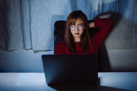 Asian woman working late at night with laptop computer home office looking screen monitor unhappy work hard sleepless, Freelancer stay home business quarantine crisis coronavirus stay home dark room.の写真素材