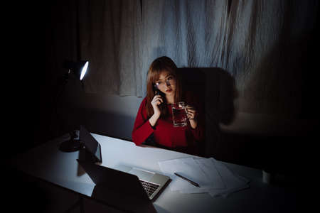 Asian woman working late time at night talking with smartphone, laptop computer home office unhappy emotion, Freelancer stay home business sleepless quarantine crisis coronavirus in dark room.の写真素材