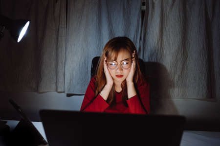 Asian woman working late at night with laptop computer home office looking screen monitor stressed work hard, Freelancer stay home business sleepless quarantine crisis coronavirus in dark room.の写真素材