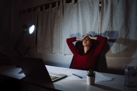 Asian woman working late at night with laptop computer home office looking screen monitor stressed work hard, Freelancer stay home business sleepless quarantine crisis coronavirus in dark room.の写真素材