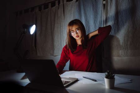 Asian woman working late at night with laptop computer home office looking screen monitor stressed work hard, Freelancer stay home business sleepless quarantine crisis coronavirus dark room.の写真素材
