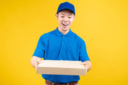 Delivery express of pizzaman asian male showing box delicious fast deliver to receiver shipping buying online order wearing blue uniform on yellow background isolated studio shot.の写真素材