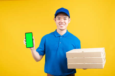 Delivery asian male presentation order pizza in box with smartphone green screen delicious fast deliver to receiver shipping buying online on yellow background isolated studio shot.の写真素材